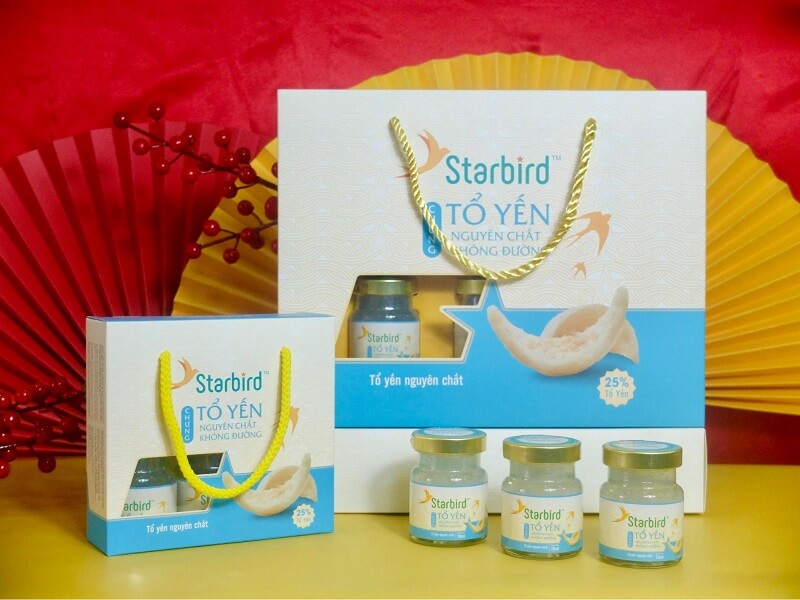 Bao bì sản phẩm tổ yến Starbird, gồm hộp lớn và nhỏ, với lọ yến nguyên chất không đường, trên nền quạt đỏ.