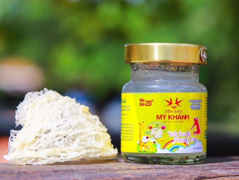 Hũ yến sào Mỹ Khánh với tổ yến tươi bên cạnh, nền xanh lá cây mờ, nhãn vàng nổi bật.
