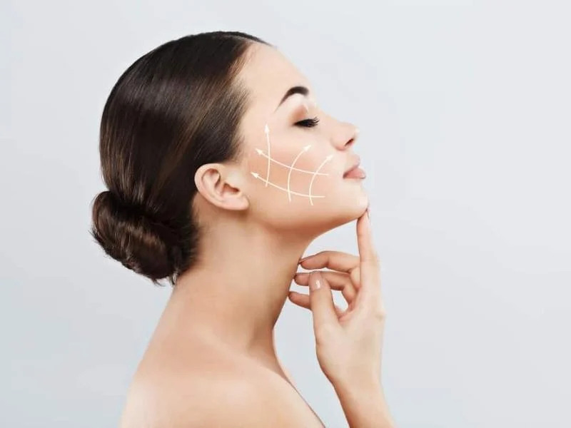 Người phụ nữ với mái tóc búi, vẽ đường nâng cơ trên má, biểu tượng của chăm sóc da và làm đẹp.