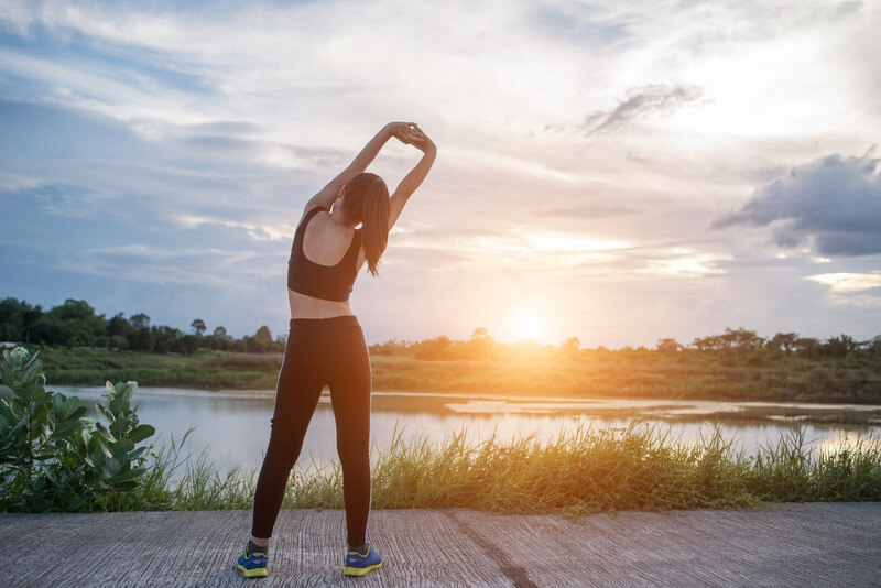 Người phụ nữ tập thể dục buổi sáng bên hồ, dưới ánh nắng bình minh, tạo cảm giác thư giãn và năng động.