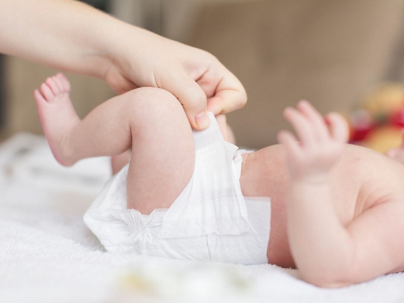 Người lớn đang thay tã cho em bé sơ sinh nằm trên giường, tạo cảm giác thoải mái và sạch sẽ cho bé.